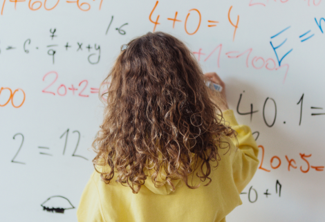 Petite fille debout devant le tableau de l'école, en cours de mathématiques.