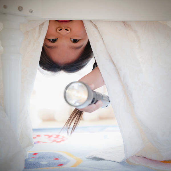 Child looking under bed with flashlight