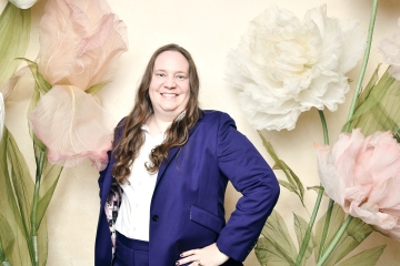 Genny Marcoux standing in front of a background of human-sized pink and white artificial flowers
