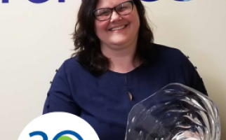 Glenda wearing a blue dress holding a glass bowl and smiling at the camera with the Let's Talk Science 30th logo in the corner