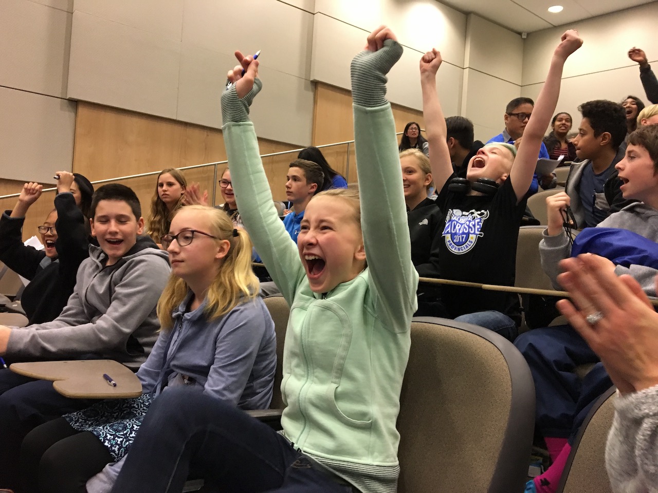 Students with arms raised, cheering at Let’s Talk Science Challenge quiz competition.