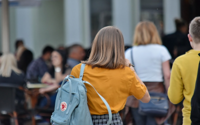 Blonde girl with backpack and ochre shirt facing away