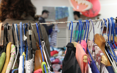 Clothing on a rack in the foreground with shoppers in the background 