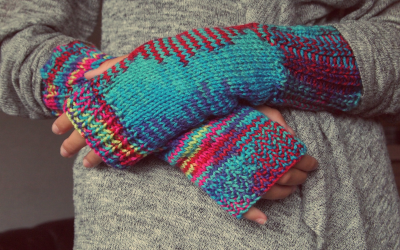 Woolen mittens on a pair of hands crossed over an abdomen.