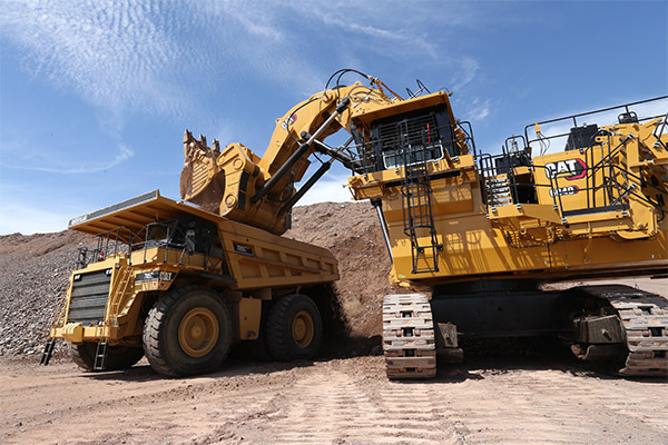 Shown is a colour photograph of two large yellow vehicles in front of a pile of gravel.