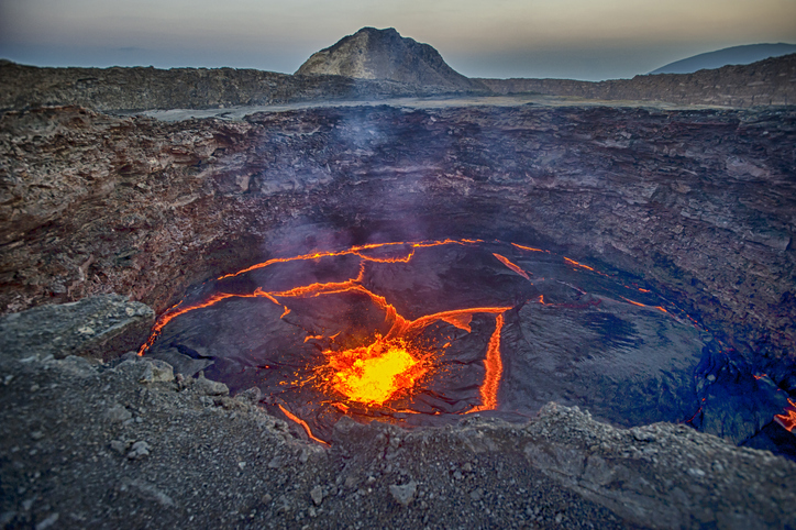 Shown is a colour photograph of a puddle of steaming, red-hot lava in a rocky landscape.