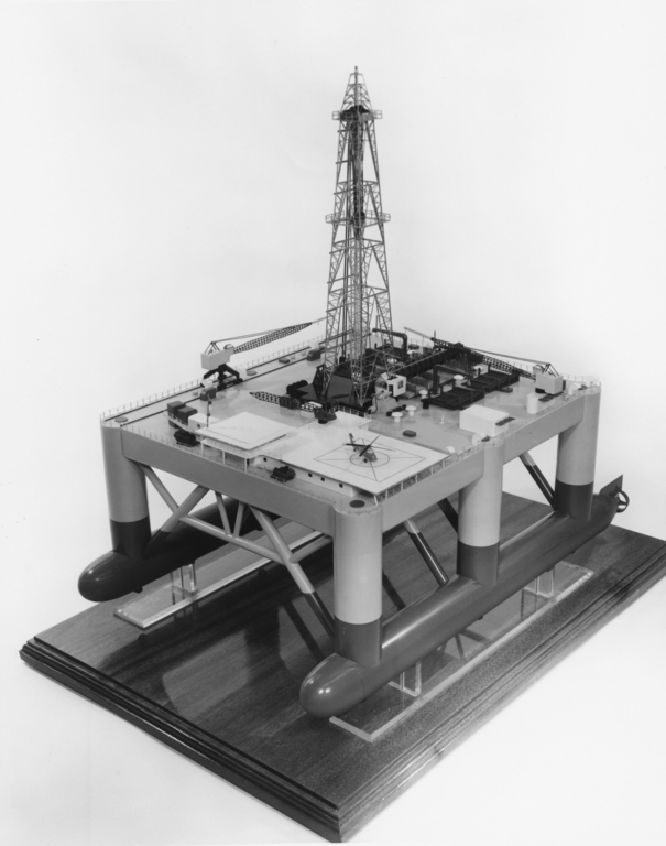 Shown is a black and white photograph of a model of a platform with six pillars and a metal tower.