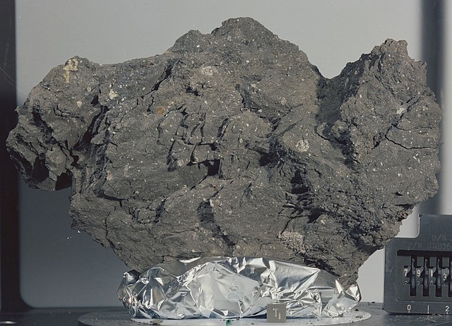 Shown is a colour photograph of a grainy, jagged, dark grey rock, sitting on silver foil.
