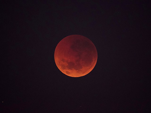 Shown is a colour photograph of the full Moon, illuminated in dark orange light.