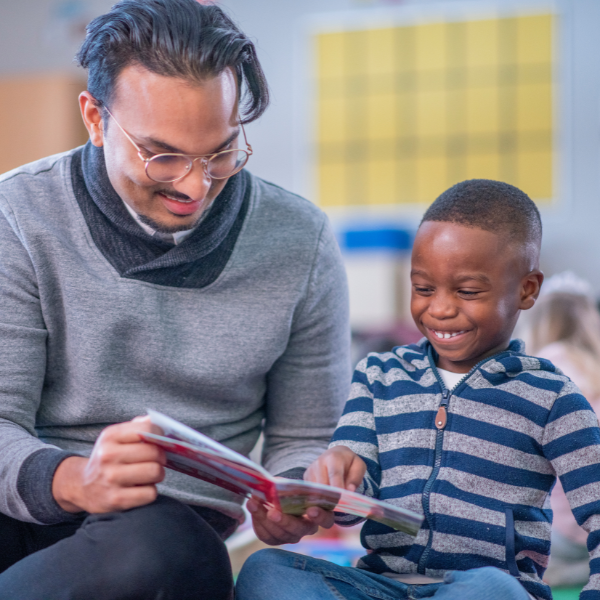 Teacher with glasses reading book with boy