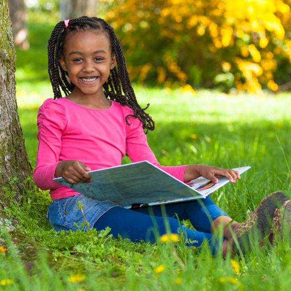 Smiling child sitting next to tree with picture book