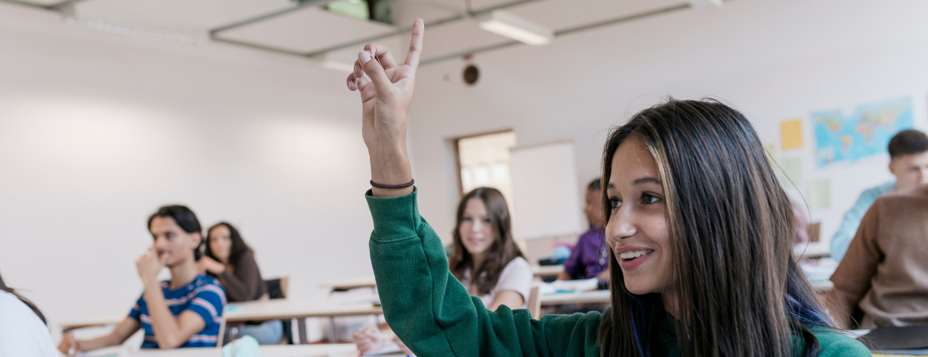 A teenager raises her hand in a classroom.