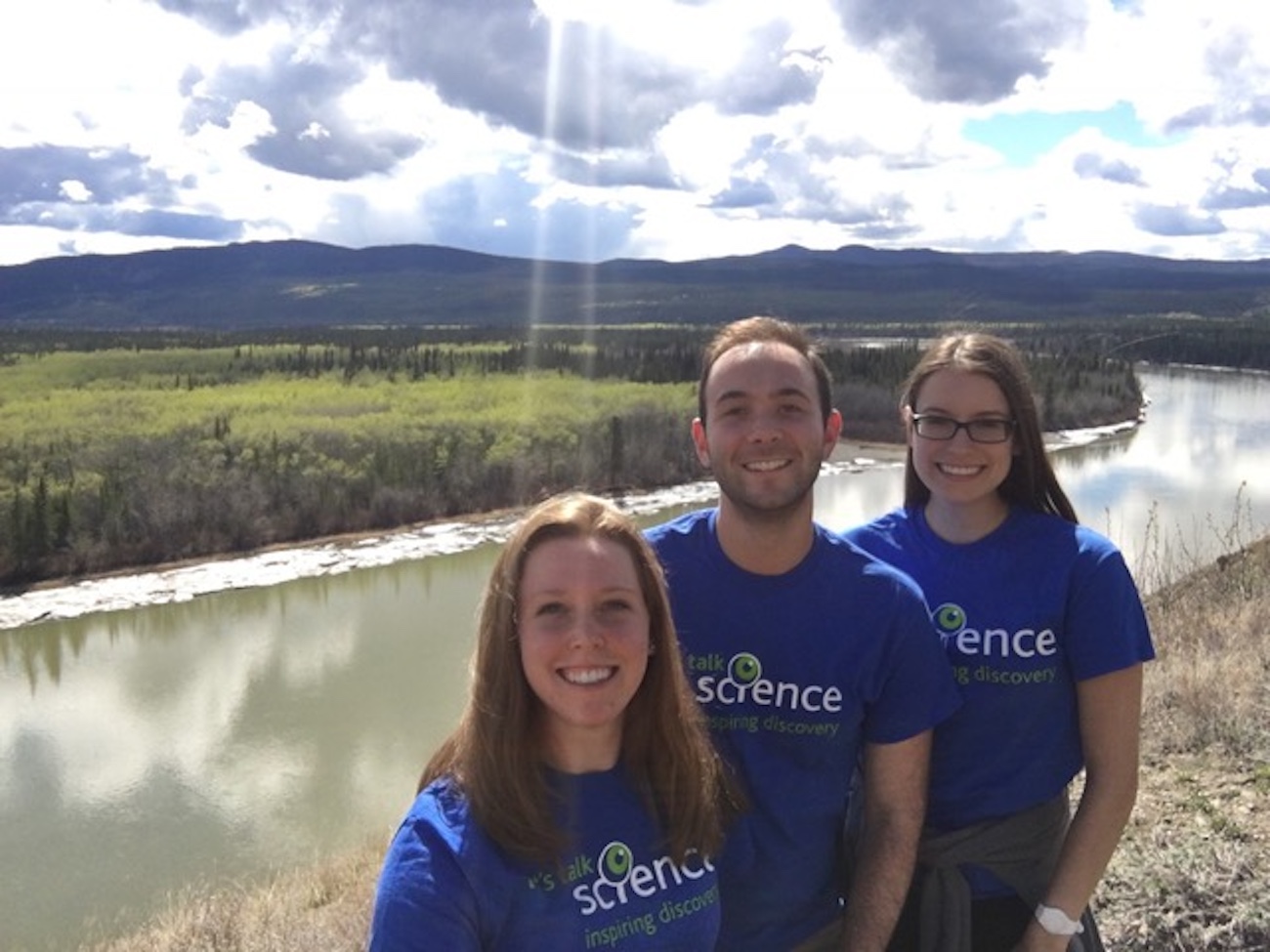 Ian Dimopoulos with other Let's Talk Science volunteers in front of a river and cloudy sky