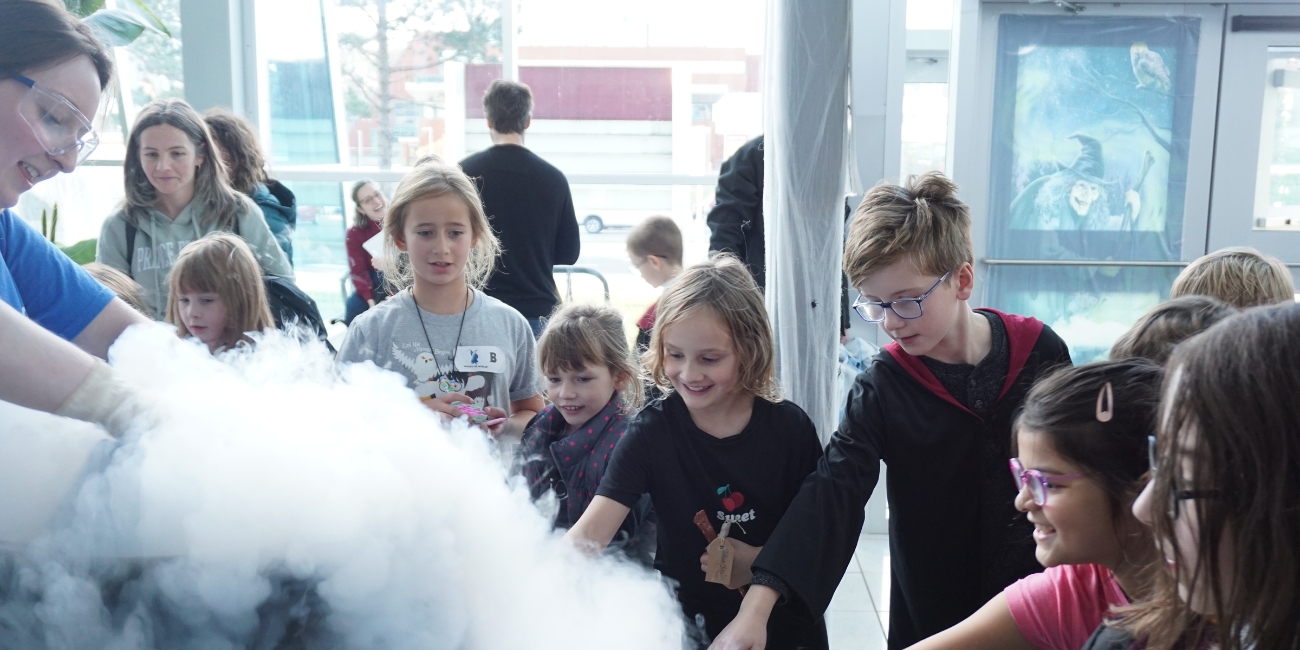 Children looking with wonder and reaching out at a science dry ice activity at the Let’s Talk Science School of Witchcraft and Wizardry at Memorial University of Newfoundland.