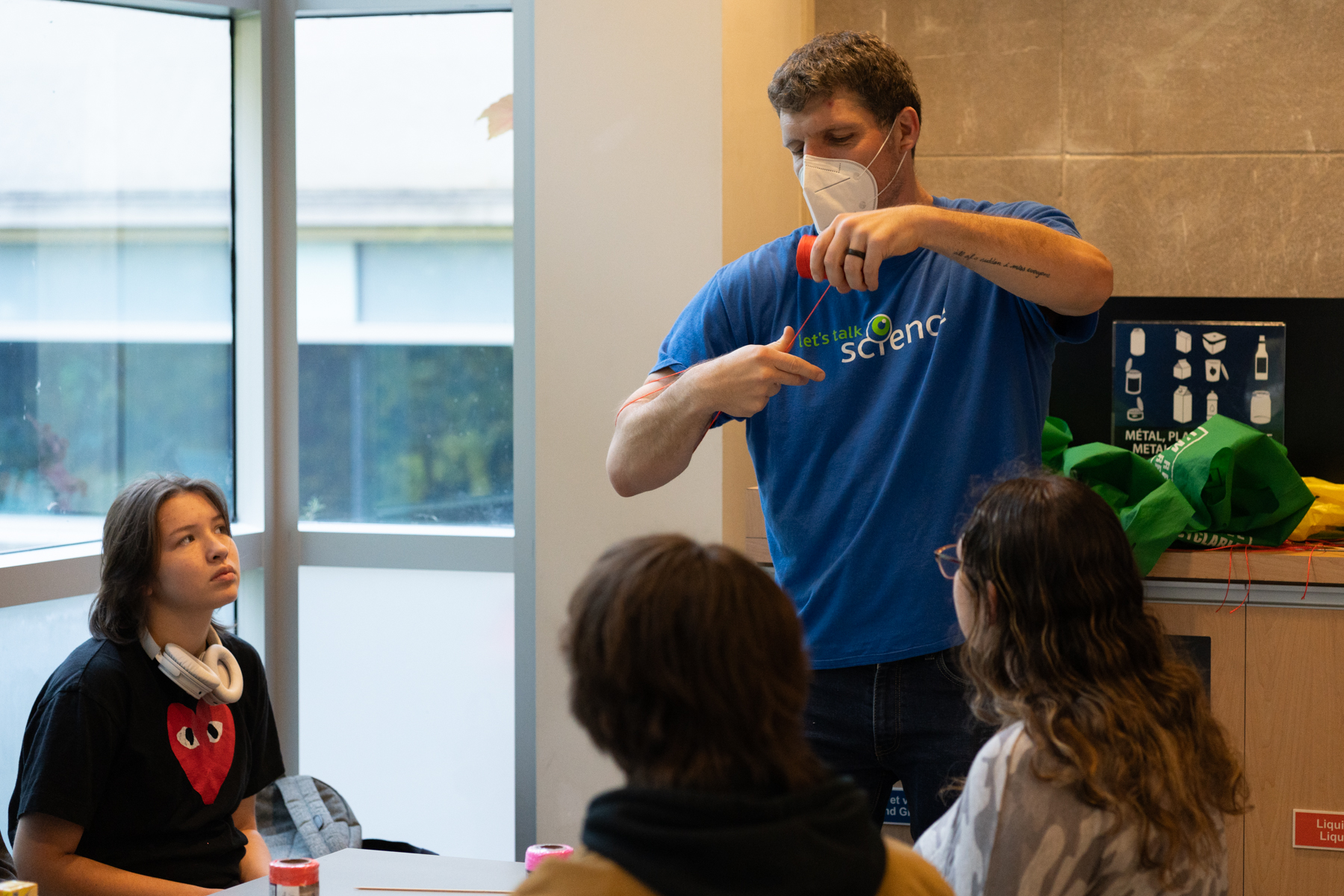 Let's Talk Science Volunteer in a blue shirt demonstrating an activity involving pink thread to attentive students