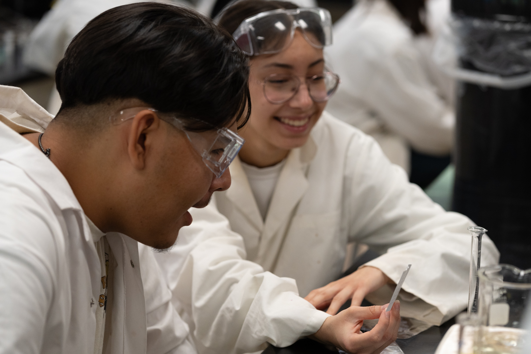 Two Moose Factory students in white lab coats performing an experiment with test tubes