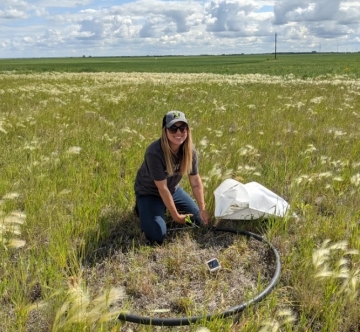 Brianna Lummerding kneeling by a plastic hoop in a grassy field collecting samples