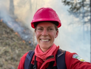 Kira Hoffman wearing red hard hat with smoke in the background