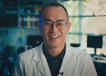 Li Tan wearing white lab coat, in his lab, smiling