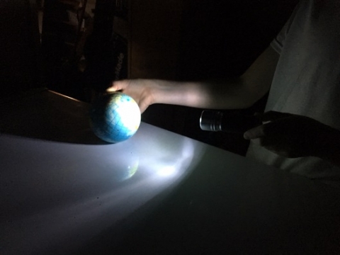 Student shining flashlight on globe 