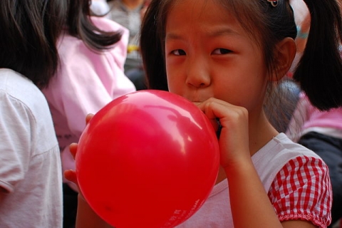 Girl blowing up a balloon/Une petite fille qui gonfle un ballon