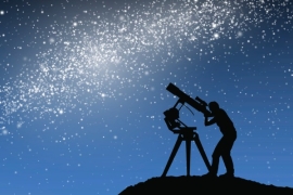 SIlhouette of a figure examining stars with a telescope