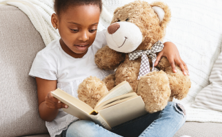 Young child reads a book with a teddy bear