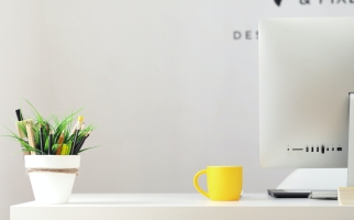 A white desk with a computer, a yellow mug, and a houseplant on it