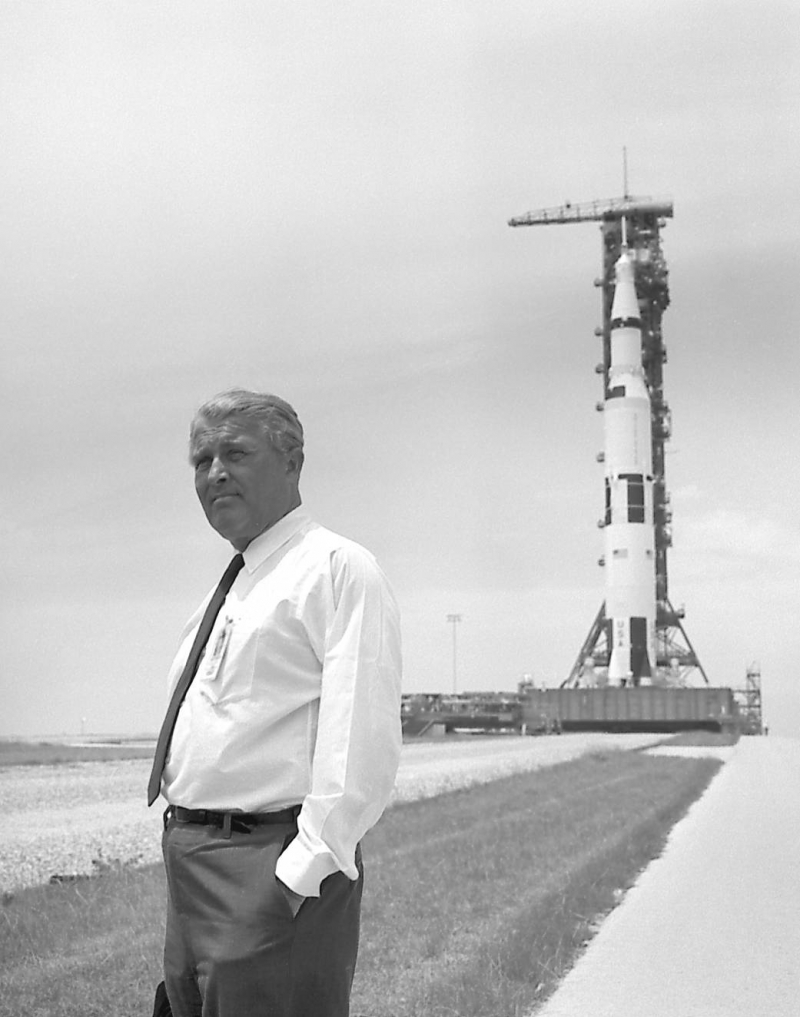Wernher von Braun, one of the most famous aerospace engineers, standing in front of his most well-known project, the Saturn V rocket