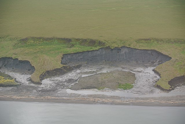 Shown is a colour photograph of land that has collapsed to show grey soil beneath.