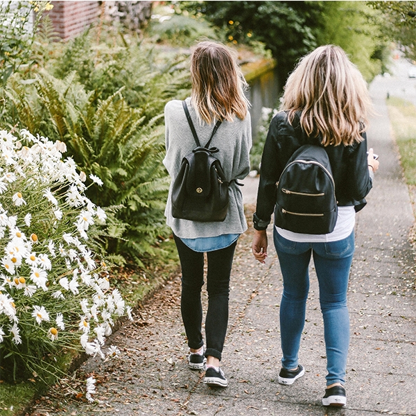 Two girls walking down a sidewalk. 