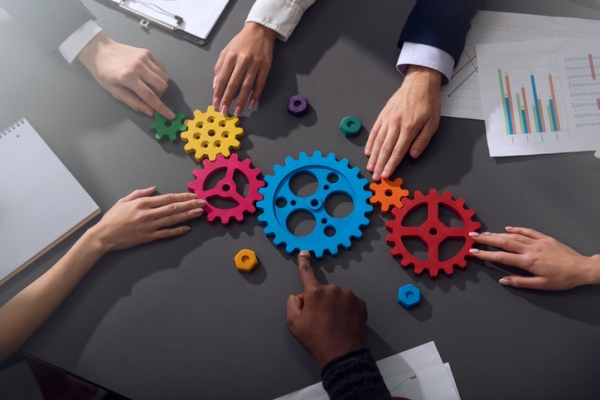 A diverse group of hands touching a set of multi-coloured gears on a table