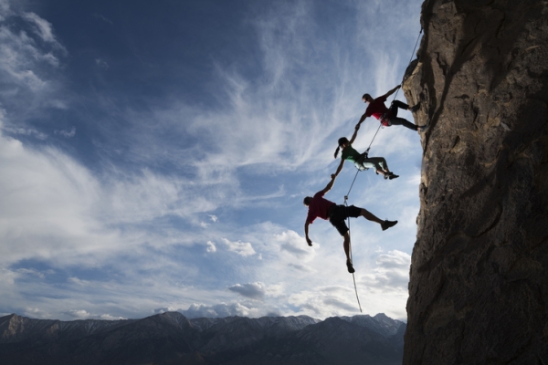 Three climbers strapped to each other climbing up a sheer cliff face