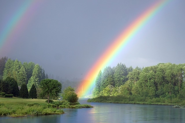 Shown is a colour photograph of a rainbow in the sky over a lake.