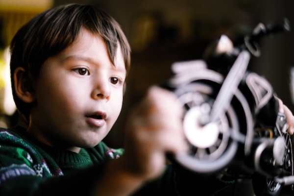 Shown is a colour photograph of a child touching the wheel of a model motorcycle.