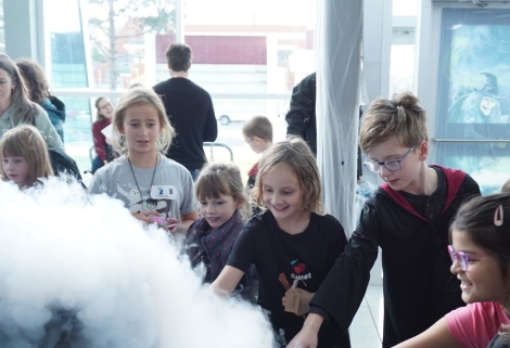 Children looking with wonder and reaching out at a science dry ice activity at the Let’s Talk Science School of Witchcraft and Wizardry at Memorial University of Newfoundland.